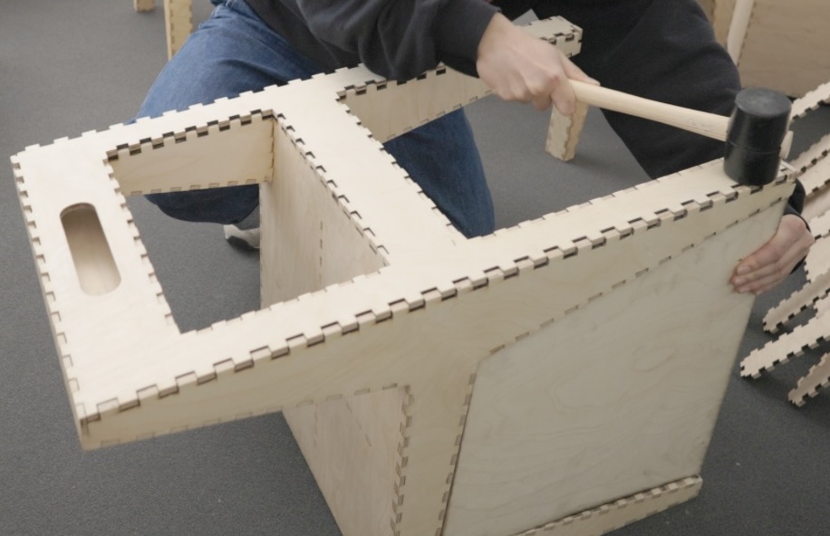 Project number 8. Mallet-Based Assembly. A person hammering on a piece of laser cut wood to assemble a chair.